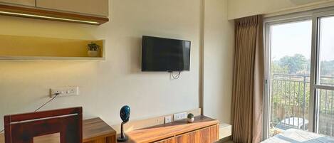 A modern bedroom with a bed, a wooden desk, a television, and a window with curtains.