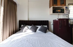 A bed with a headboard, a wardrobe, and a microwave above it. - Studios By Ritumbhara (Jaipur)