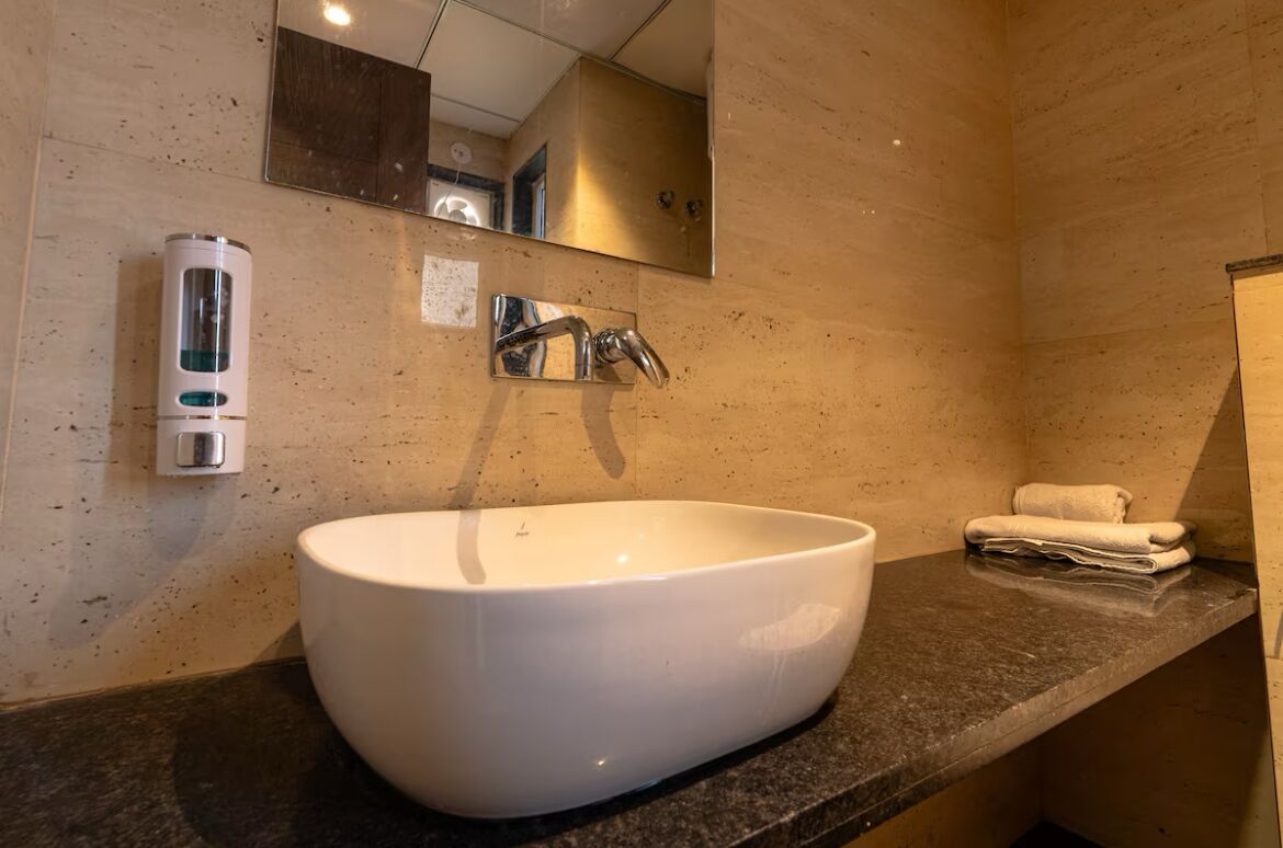 Une salle de bain avec un grand lavabo blanc, un miroir, un porte-serviettes et un distributeur de savon.