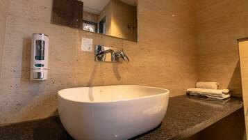 Une salle de bain avec un grand lavabo blanc, un miroir, un porte-serviettes et un distributeur de savon.