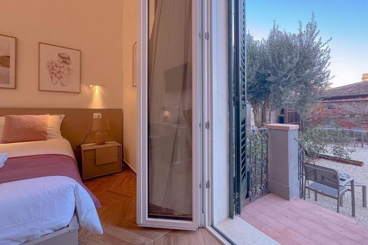 A bedroom with a bed, nightstand, and a sliding glass door leading to an outdoor area with a bench and a table.