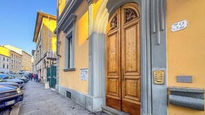 A street with parked cars, a yellow building with a large wooden door, and a mailbox labeled 'PUBBLICITÀ'. - In Corte - Rooms in Florence (Florence)