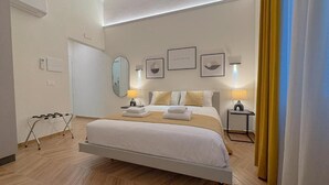 A modern hotel room with a large bed, bedside lamps, a mirror, and framed artwork on the wall. - In Corte - Rooms in Florence (Florence)