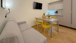 A modern living room with a sofa, a dining table with yellow chairs, a flat-screen TV mounted on the wall, and a kitchen area in the background. - In Corte - Rooms in Florence (Florence)