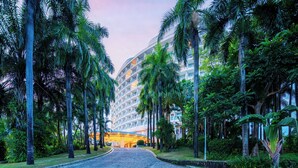 Un hotel con una entrada curva, palmeras y un edificio moderno con balcones.