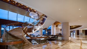 Un moderno vestíbulo de hotel con una escalera espiral, ventanas amplias y una lámpara central.