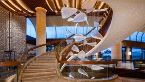 Un interior moderno con una escalera espiral, una instalación de luces colgantes y una barandilla de vidrio.