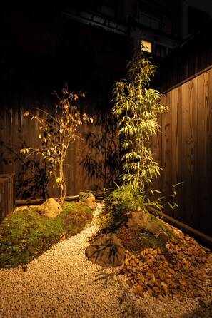 Un jardín con una planta de bambú, rocas y una valla de madera.