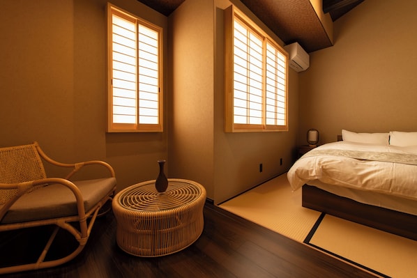 A traditional Japanese-style bedroom with tatami flooring, a low bed, a wooden chair, and a small round table.