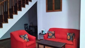 A staircase with wooden railings, a red sofa with patterned cushions, a small table, and a window with two panes. - Dorade Double Room – Cozy Stay at Alto do Fortim B&B (Mindelo)
