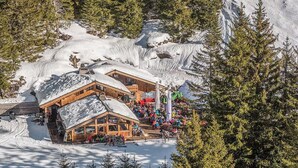 Una cabana de fusta amb un teulat cobert de neu, envoltada d'arbres i neu.