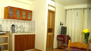 A compact kitchen with wooden cabinets and a dining area with a table and chairs. - LA CASA DE VIDA (Cusco)