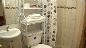 A bathroom with a toilet, a shelf with towels, a sink, and a shower curtain with a circular pattern. - LA CASA DE VIDA (Cusco)
