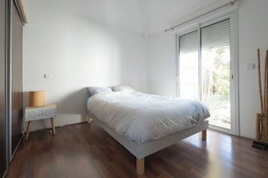 Une chambre à coucher comprenant un lit, une table de chevet, une lampe et une porte-fenêtre coulissante donnant sur l’extérieur.