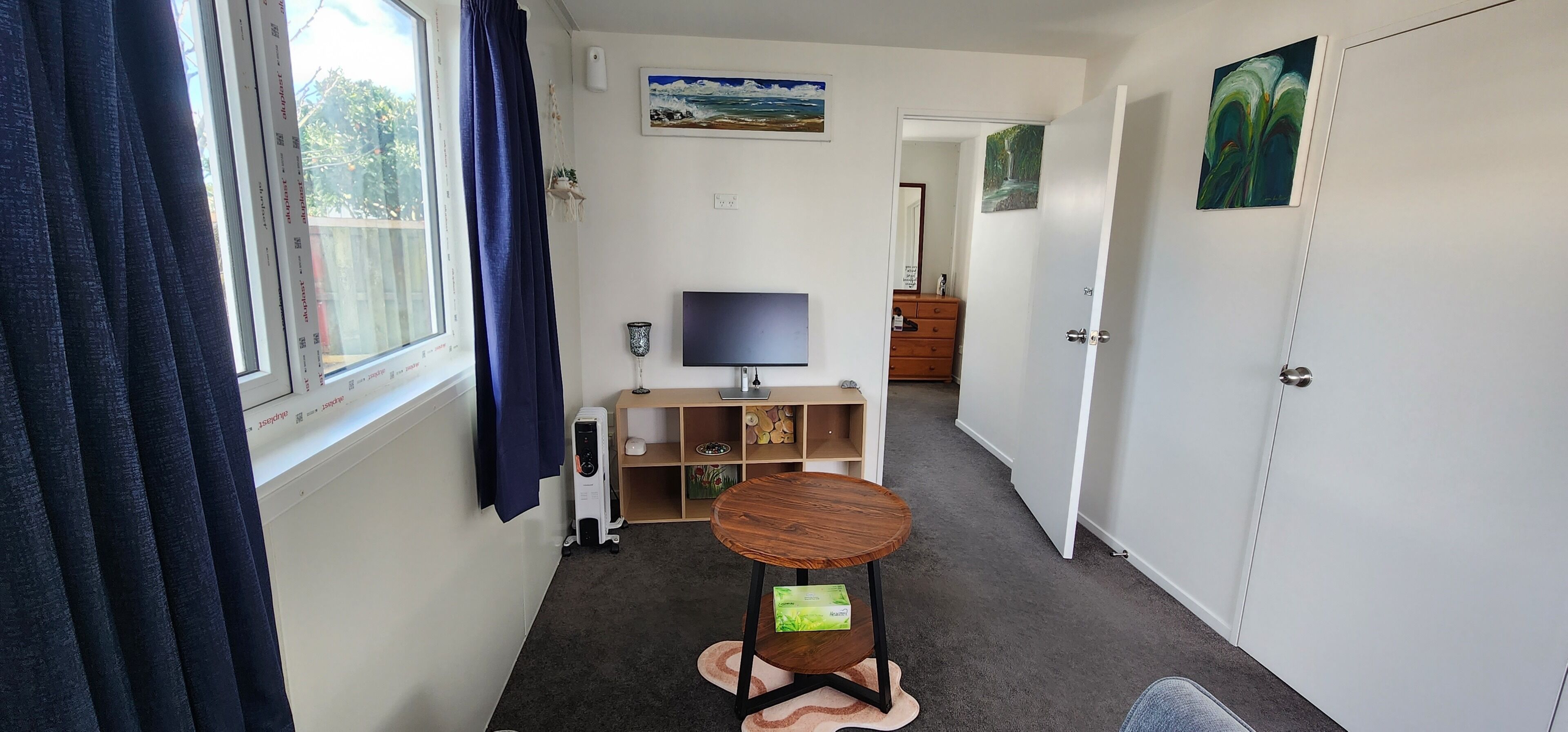 Un pasillo estrecho con una ventana, un televisor, una mesita y un armario.