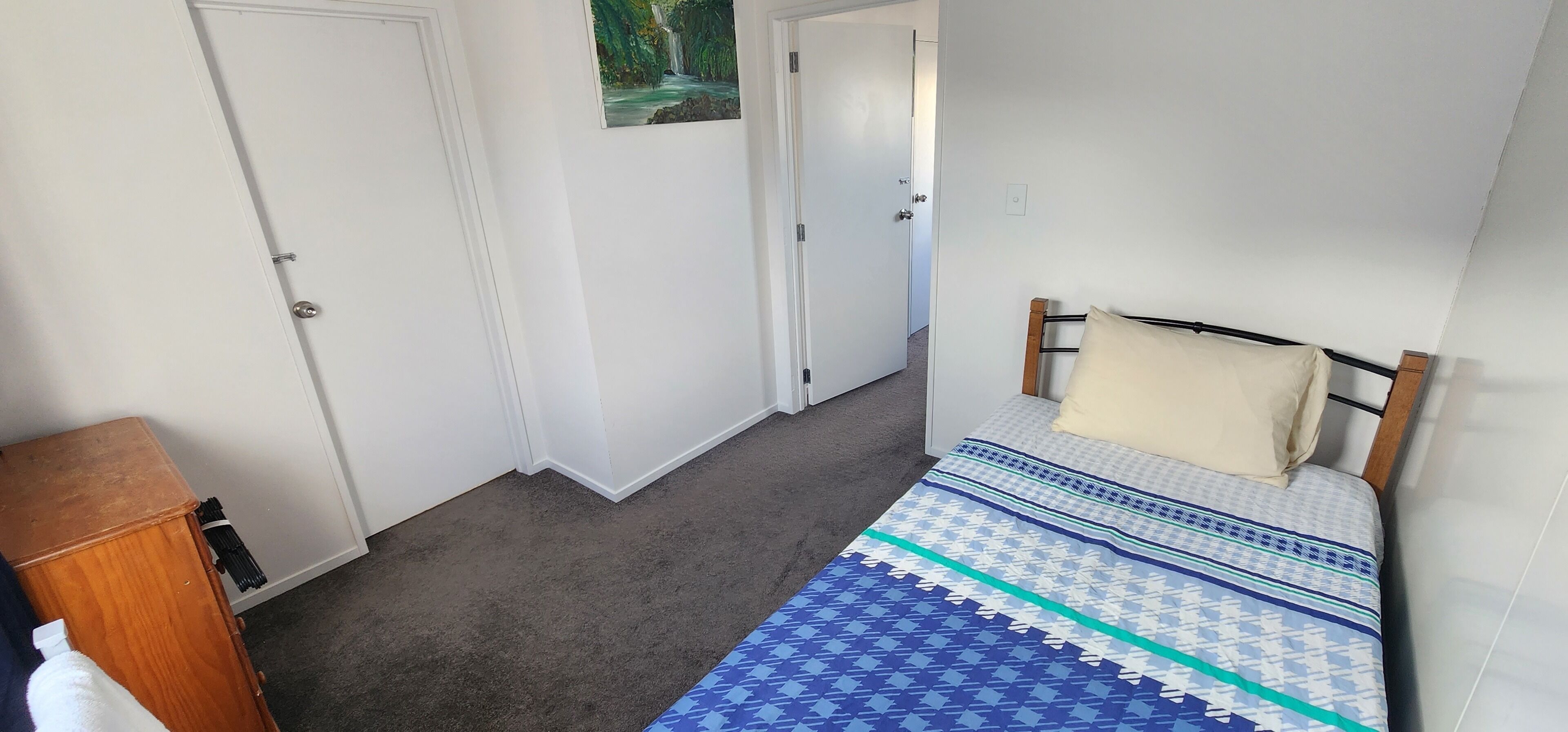 Ein Schlafzimmer mit einem Bett, einem hölzernen Kopfteil, einem Wandbild und einer Tür.