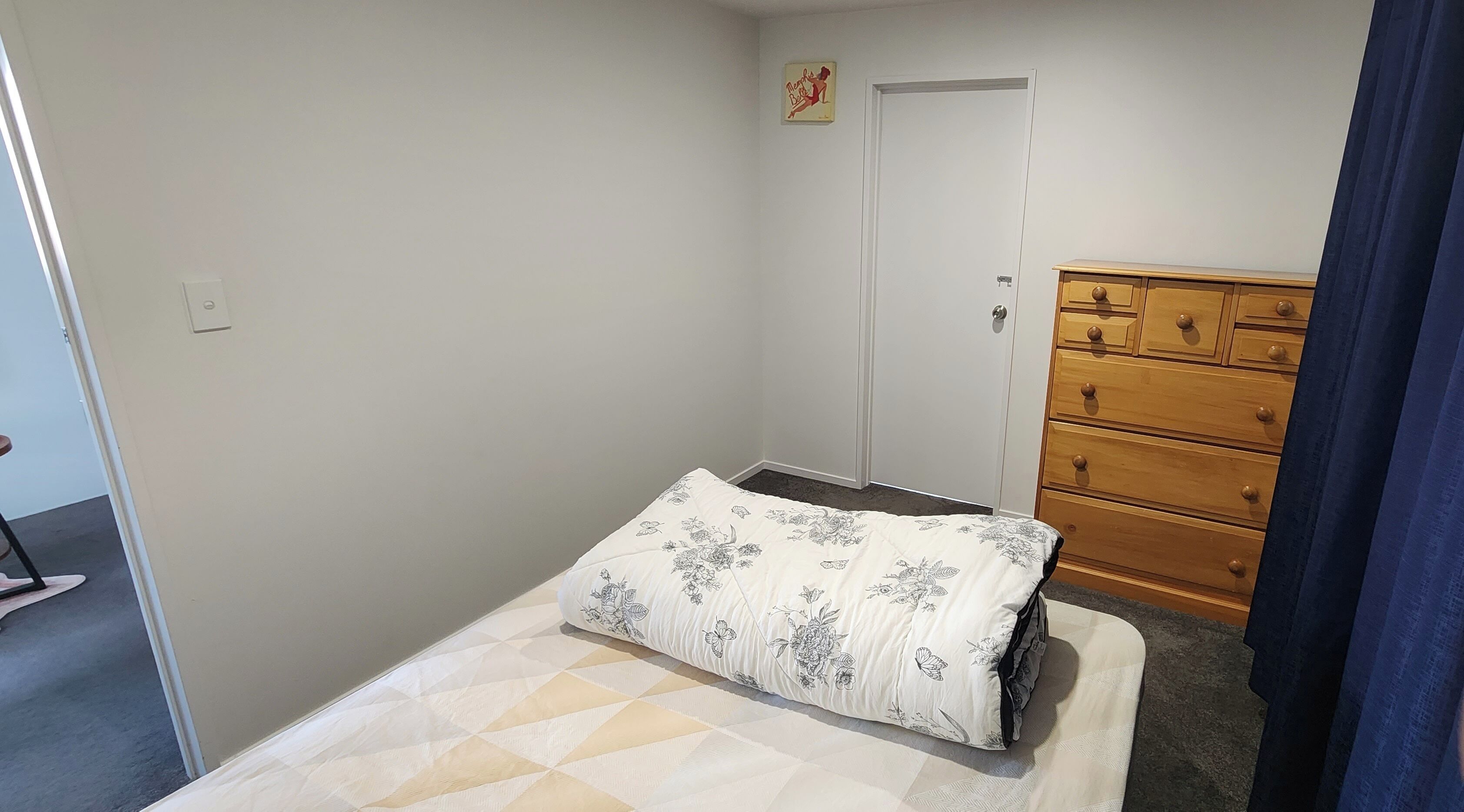 A small bedroom with a single bed, a wooden dresser, and a door.