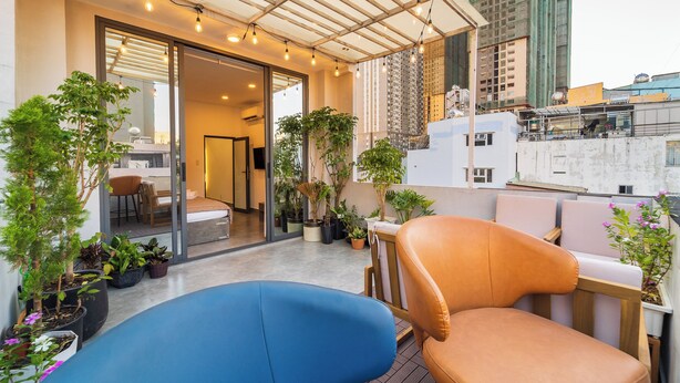 Una terraza en la azotea con un sofá azul, una silla naranja y plantas en macetas.