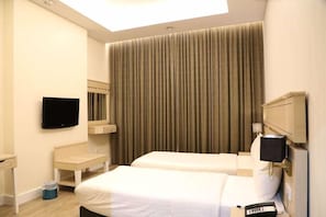 A hotel room with two beds, a TV, a desk, a chair, a trash bin, and a large window with curtains. - Wescott Plaza Hotel Apartments L.l.c (Dubai)