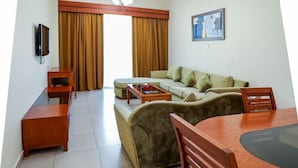 A living room with a sofa, a coffee table, a TV, and a painting on the wall. - Wescott Plaza Hotel Apartments L.l.c (Dubai)