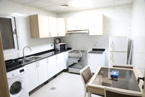 A compact kitchen with a washing machine, microwave, stove, and refrigerator. - Wescott Plaza Hotel Apartments L.l.c (Dubai)