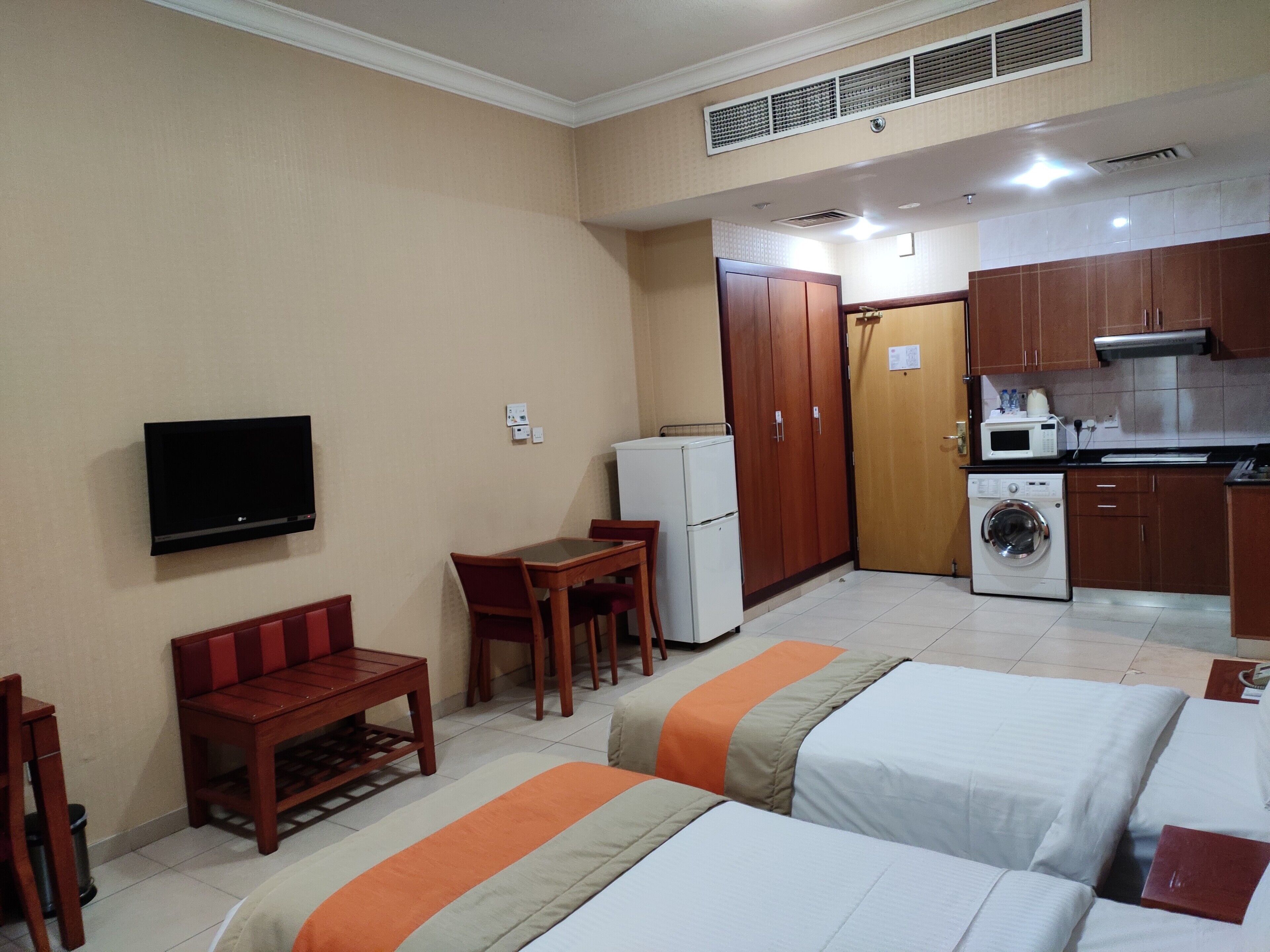 Habitación de hotel con televisión, pequeña mesa de comedor, sofá, lavadora y kitchenette.