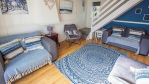 Een woonkamer met een zithoek, een getextureerd vloerkleed, een stoel en een trap.