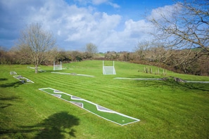 A well-maintained grassy field with goalposts and a soccer goal, surrounded by trees and a clear sky.