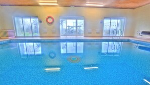 Une piscine intérieure avec des parois en verre transparent, une bouée de sauvetage et une vue sur un pont à l’extérieur.