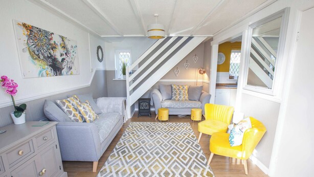 Un salon moderne avec un canapé, des fauteuils jaunes, un tapis à motifs et un escalier menant à une autre pièce.