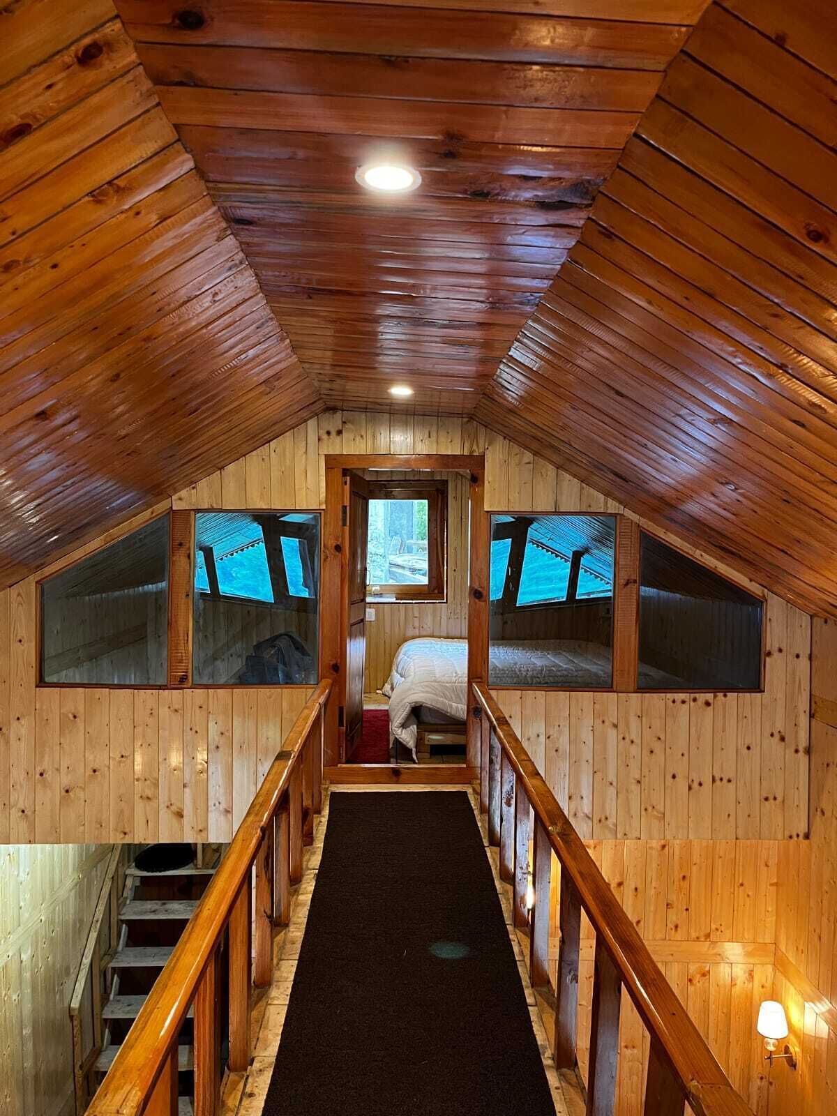 A wooden interior with a staircase, a bed, and windows.