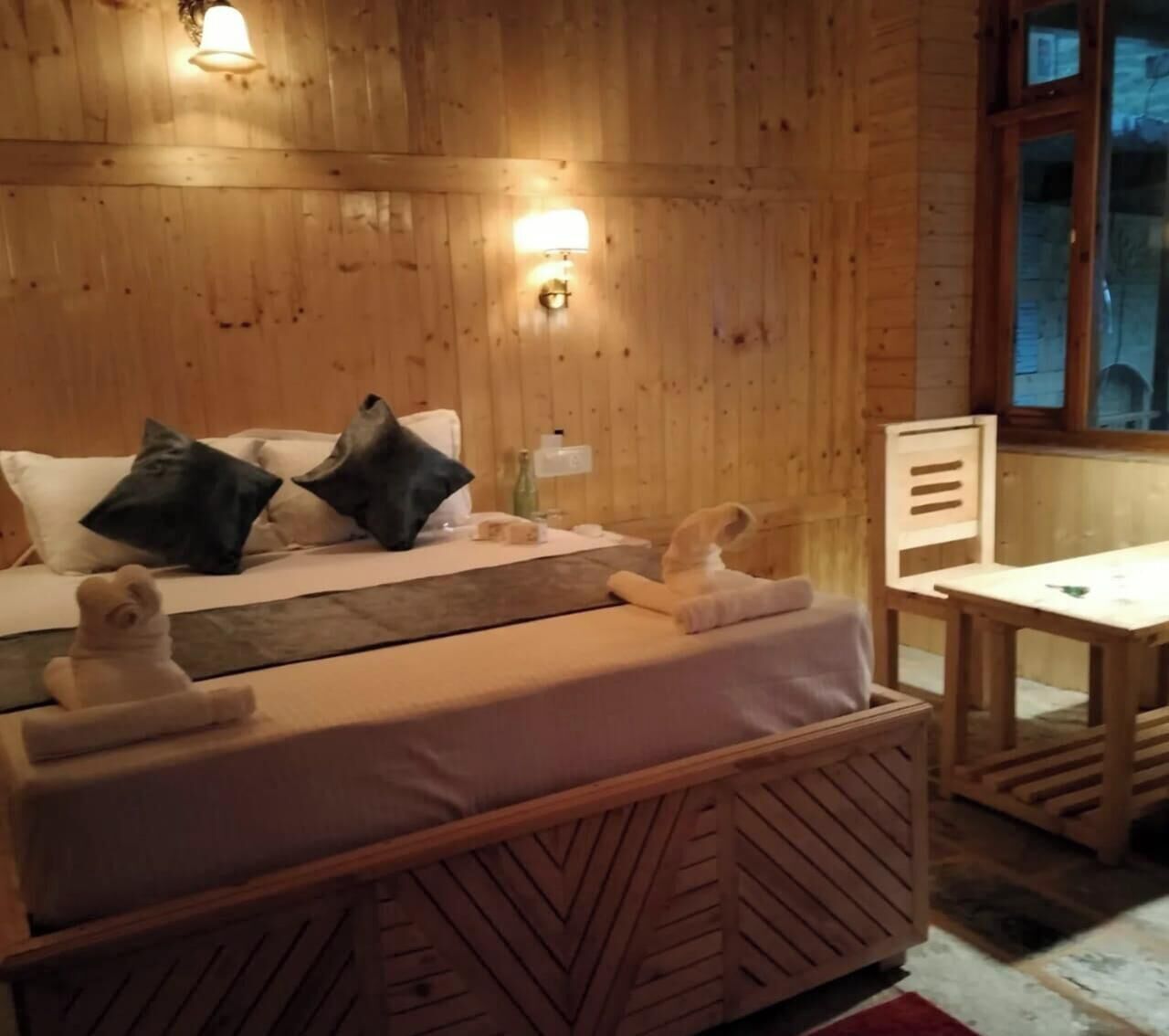 A wooden cabin-style room with a bed, bedside table, and a small table with a chair.
