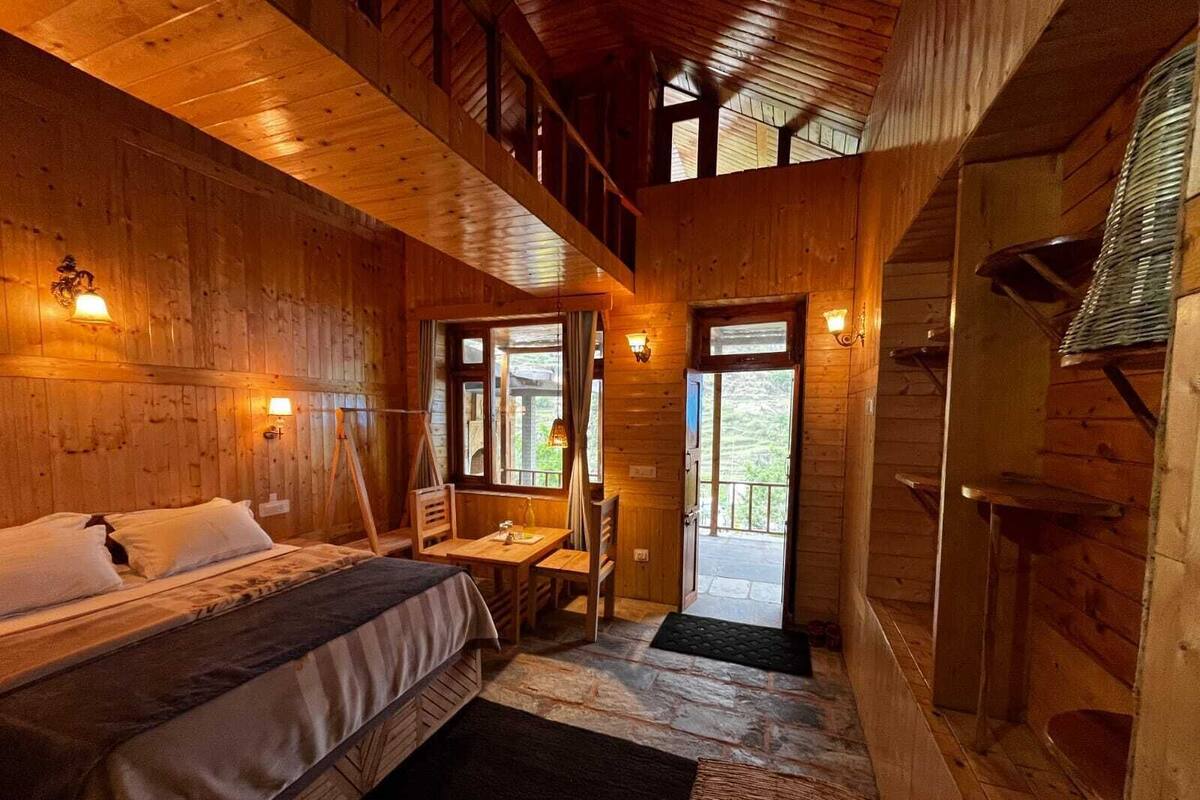 Una cabaña de madera con una cama, una mesa y una silla. Cuenta con un balcón con vistas al exterior.