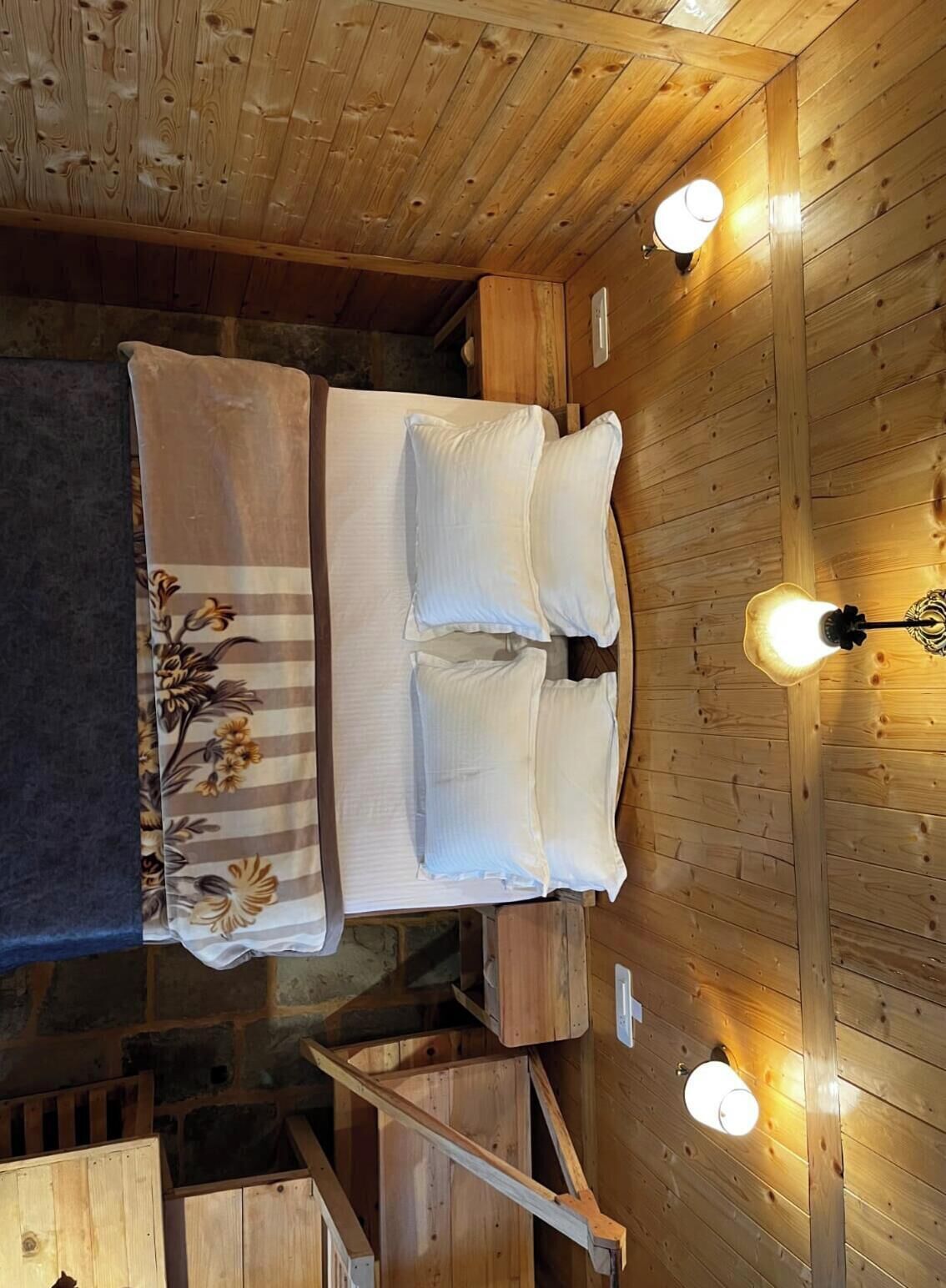 A wooden cabin-style room with a bed, two wall-mounted lights, and a wooden staircase.