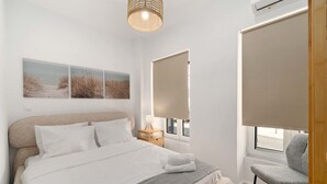 A bedroom with a bed, bedside table, lamp, window with blinds, and a chair. - Kastella Retreat | Private Terrace + Yard | 2BR | Professionally Managed | Piraeus Seafront District (Piraeus)