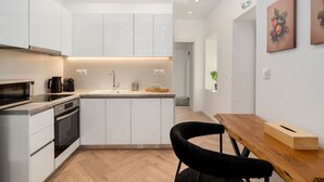 A modern kitchen with white cabinets, a wooden dining table, and a black chair. - Kastella Retreat | Private Terrace + Yard | 2BR | Professionally Managed | Piraeus Seafront District (Piraeus)