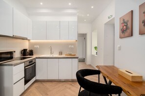 A modern kitchen with white cabinets, a wooden dining table, and a black chair. - Kastella Retreat | Private Terrace + Yard | 2BR | Professionally Managed | Piraeus Seafront District (Piraeus)