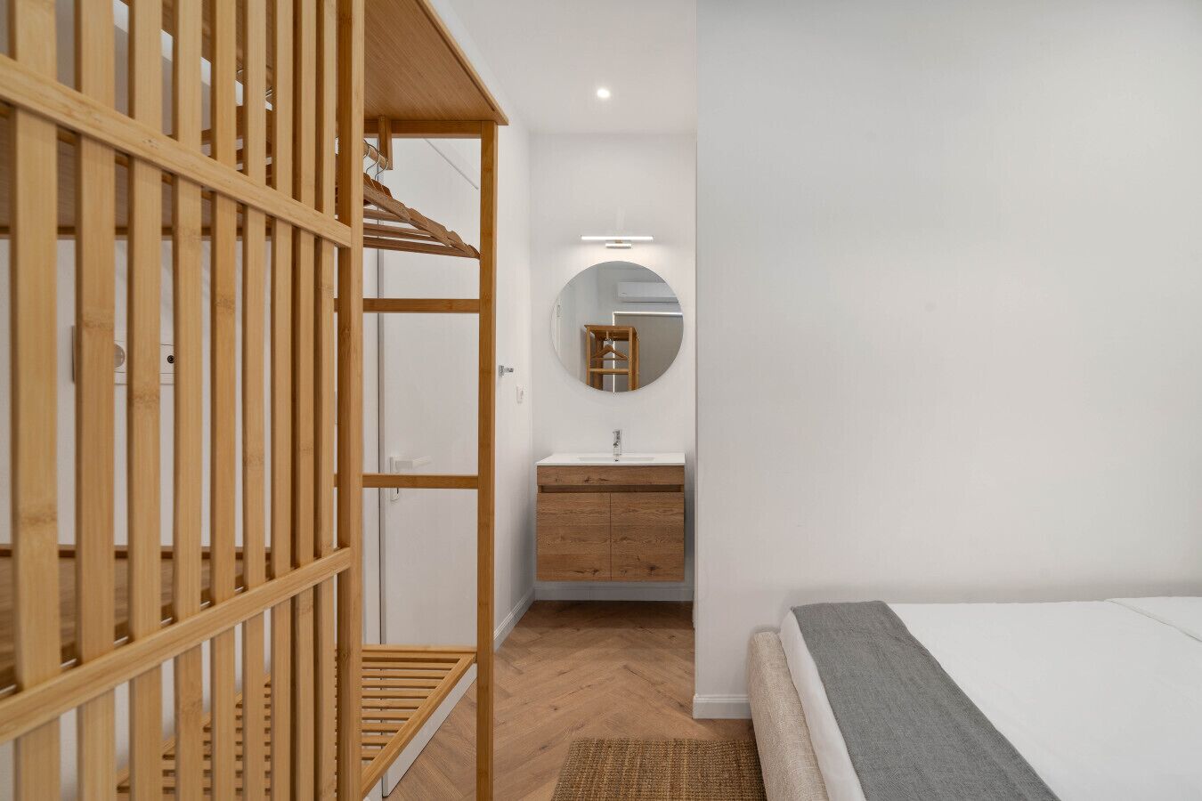 A bedroom with a wooden bunk bed, a bedside table, a mirror, and a small bathroom with a sink and cabinet.