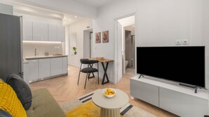 A modern living room with a flat-screen TV, a dining area with a table and chairs, and a kitchen with white cabinets and a built-in oven. - Kastella Retreat | Private Terrace + Yard | 2BR | Professionally Managed | Piraeus Seafront District (Piraeus)