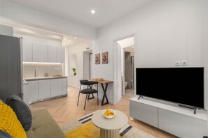 A modern living room with a flat-screen TV, a dining area with a table and chairs, and a kitchen with white cabinets and a built-in oven. - Kastella Retreat | Private Terrace + Yard | 2BR | Professionally Managed | Piraeus Seafront District (Piraeus)