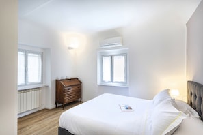 Un dormitorio con cama, cómoda, dos ventanas y un equipo de aire acondicionado.