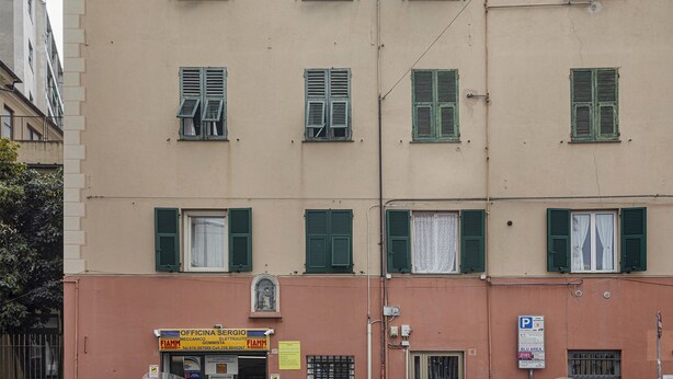 A multi-story building with green shutters on windows, a visible storefront with signage, and a parking sign indicating a parking area. - Cute Nest Near the Center by Wonderful Italy (Genoa)