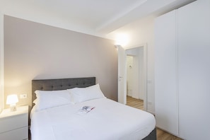 Una cama bien hecha con sábanas blancas, una lámpara de noche y una revista sobre la cama.