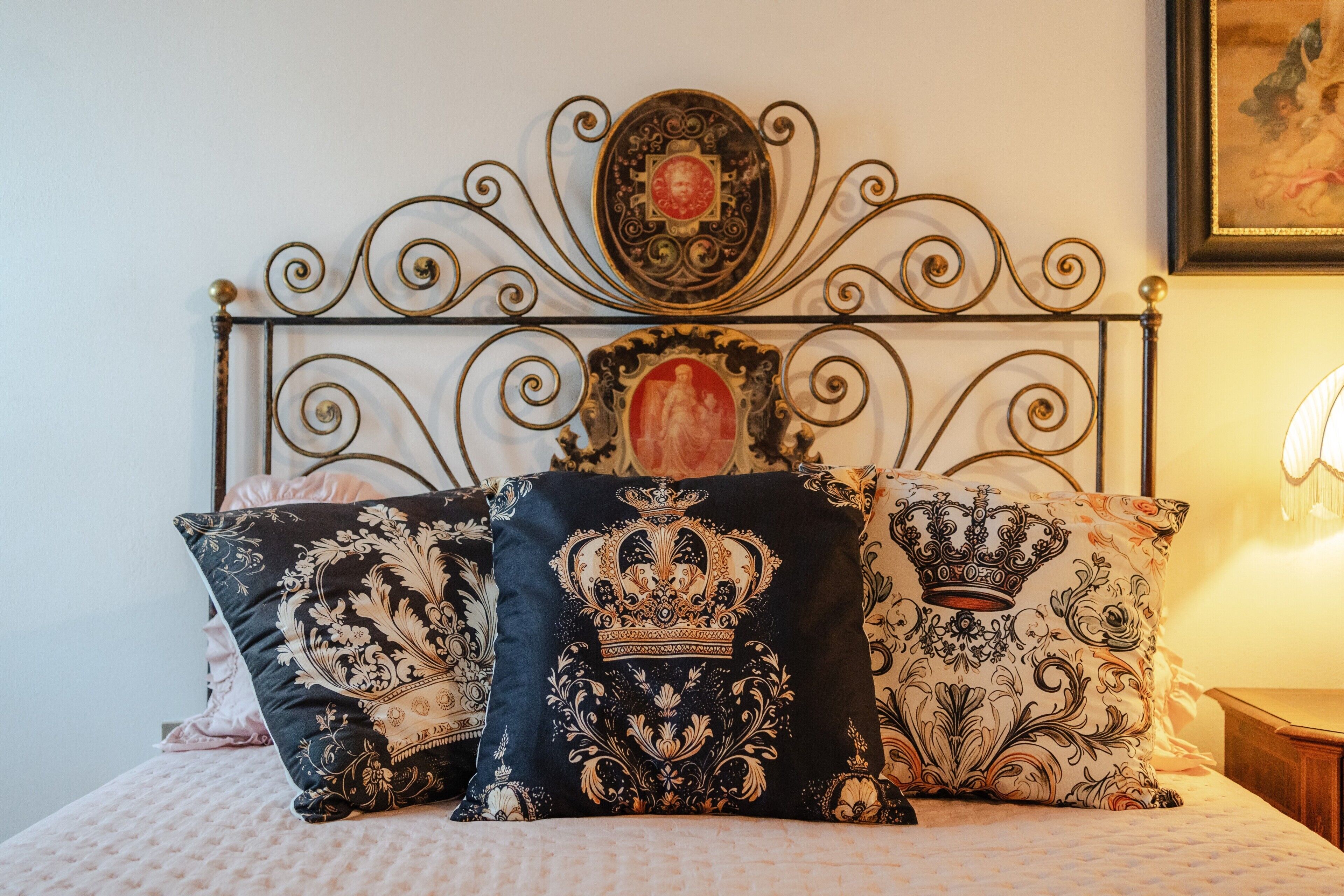 Un letto con testiera in metallo decorata, cuscini ornamentali e un quadro appeso sopra.. Villa Maria Casa Vacanze a Cetinale tra le colline
