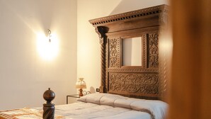 Ein Schlafzimmer mit einem hölzernen Kopfteil, einem Bett mit einer Quilttdecke, einem Nachttisch mit einer Lampe und einer Wandleuchte.
