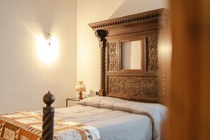 A bedroom with a wooden headboard, a bed with a quilt, a nightstand with a lamp, and a wall-mounted light.