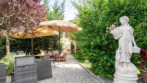 Ein Garten mit einer Statue, Korbmöbeln und einem Reetdachschirm.