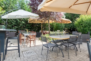 Patio esterno con tavoli e sedie, immerso nel verde.