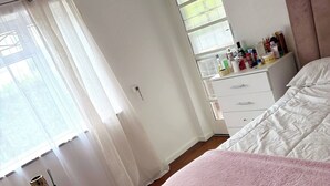 Una camera da letto con un letto, una cassettiera, una finestra con persiane, un termosifone e un tavolino con un vaso.