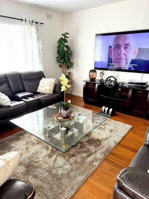 Una sala de estar con una mesa de centro de vidrio, un sofá, un televisor y una planta.